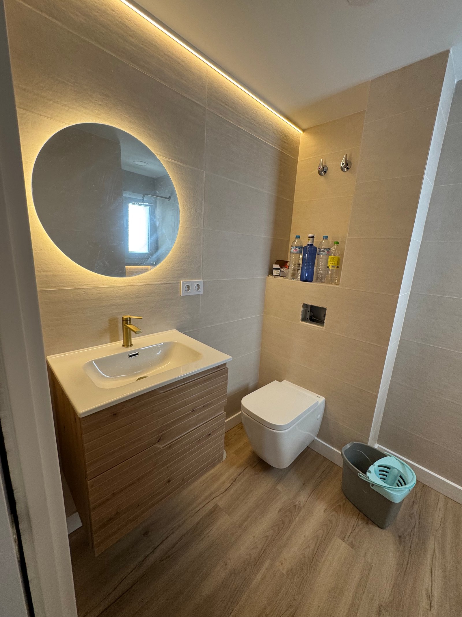 Mueble de baño con espejo retroiluminado y grifería en latón en una reforma en Sevilla